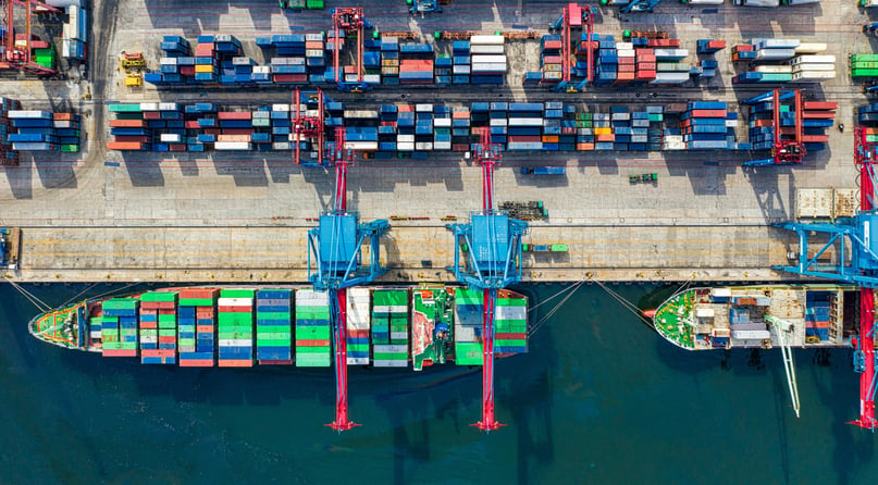 Aerial view of a busy cargo port with container ships and cranes.